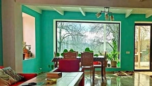 A room with teal walls, a wooden dining table, and chairs. There is a window with a view of trees outside.
