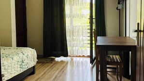 A room with a bed, a wooden table, a chandelier, and a window with curtains.