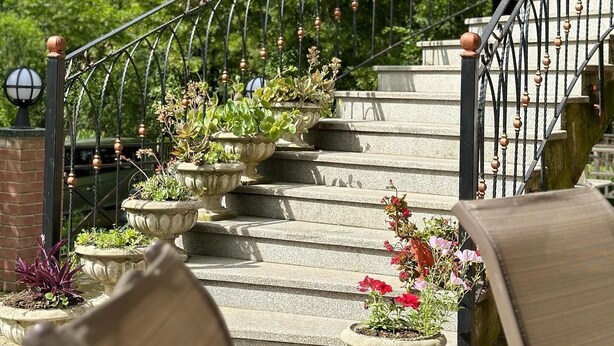 A stone staircase with metal railings, surrounded by potted plants and flowers.