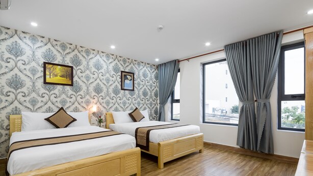 Una habitació d'hotel amb dos llits de fusta, un fons de pantalla amb dibuixos, una finestra gran amb cortines i vista a la ciutat.