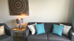 A modern living room with a grey sofa, two side chairs, a wooden side table with a lamp, and a large abstract painting on the wall. - Pretty Properties - 30 Chaldron Court (Darlington)