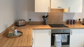 A modern kitchen with wooden cabinets, a black stove, and a toaster. There are bags of groceries on the counter. - Pretty Properties - 30 Chaldron Court (Darlington)
