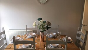 A dining table set with white plates, bowls, and cutlery, surrounded by white chairs, with a vase of flowers in the center. - Pretty Properties - 30 Chaldron Court (Darlington)