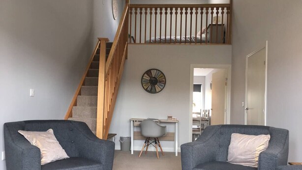 A living room with two grey armchairs, a wooden staircase, and a desk with a chair. - Pretty Properties - 30 Chaldron Court (Darlington)