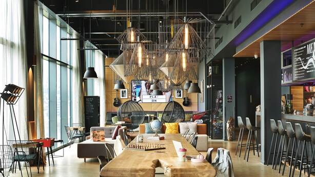 A modern bar/lounge area with a long wooden table, multiple hanging light fixtures, and a bar counter with stools.