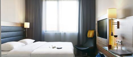 Una habitación de hotel con cama, una silla, un televisor y un escritorio con lámpara.