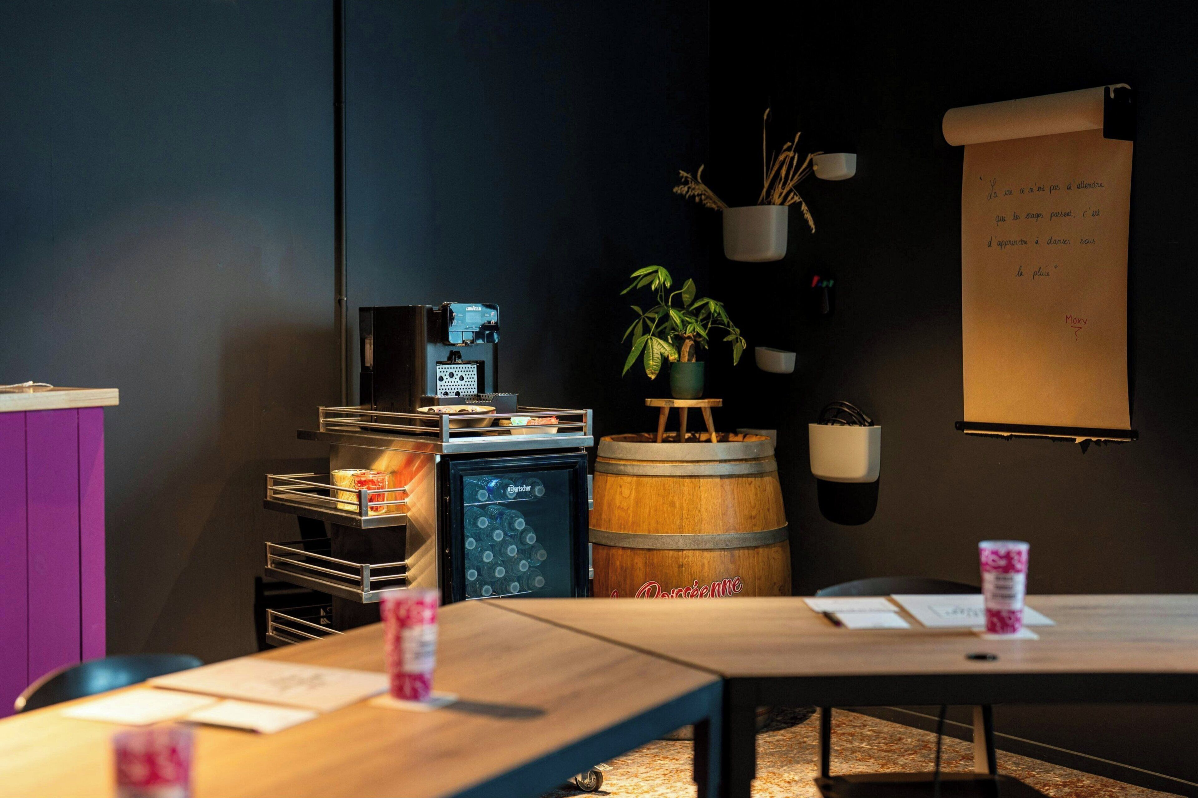 A cozy room with a wooden table, a small refrigerator, a potted plant, and a chalkboard with writing.