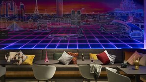 A modern lounge area with a neon cityscape mural, comfortable seating, and a bar area.