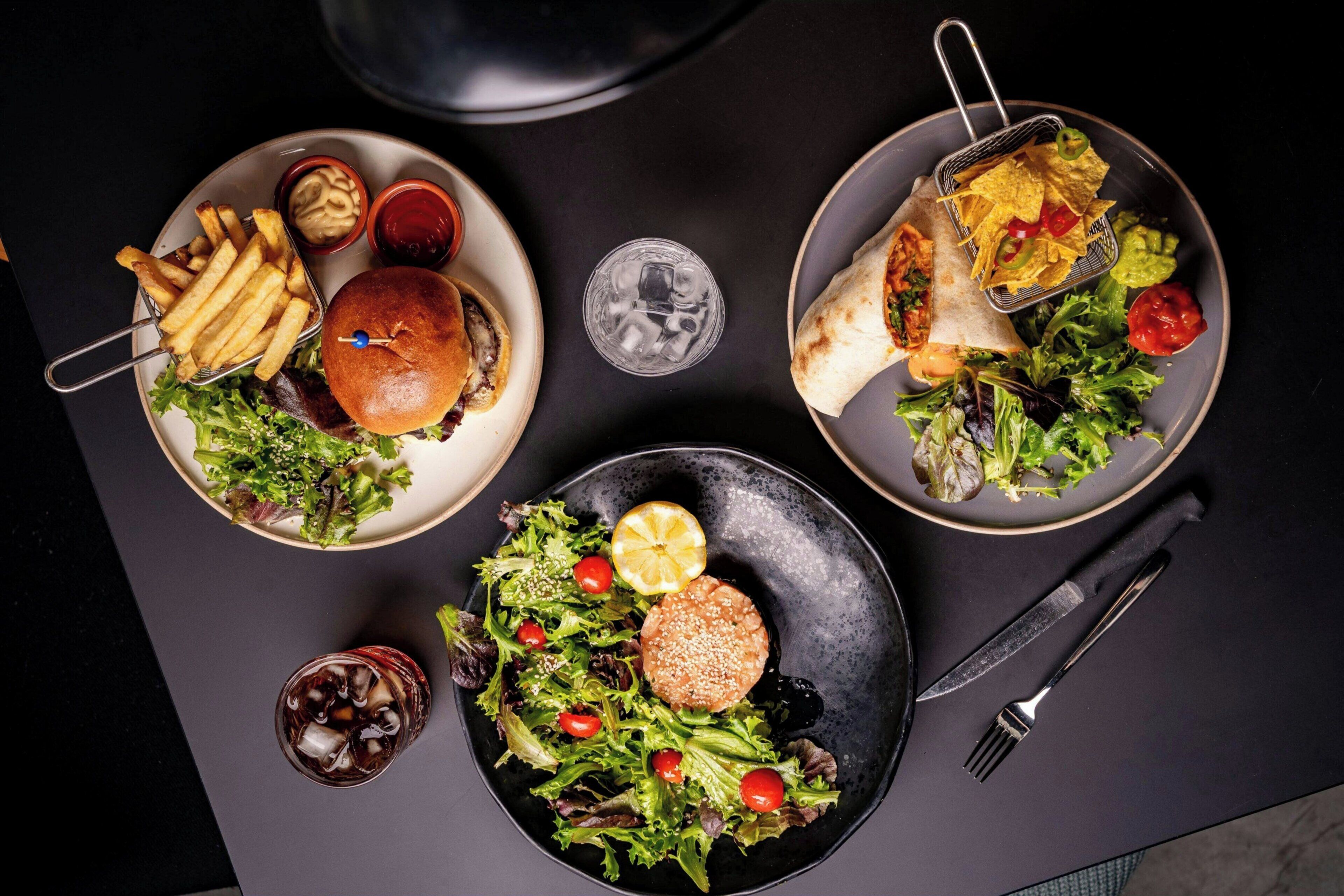 A dining table with three plates of food, a glass of iced drink, and cutlery.