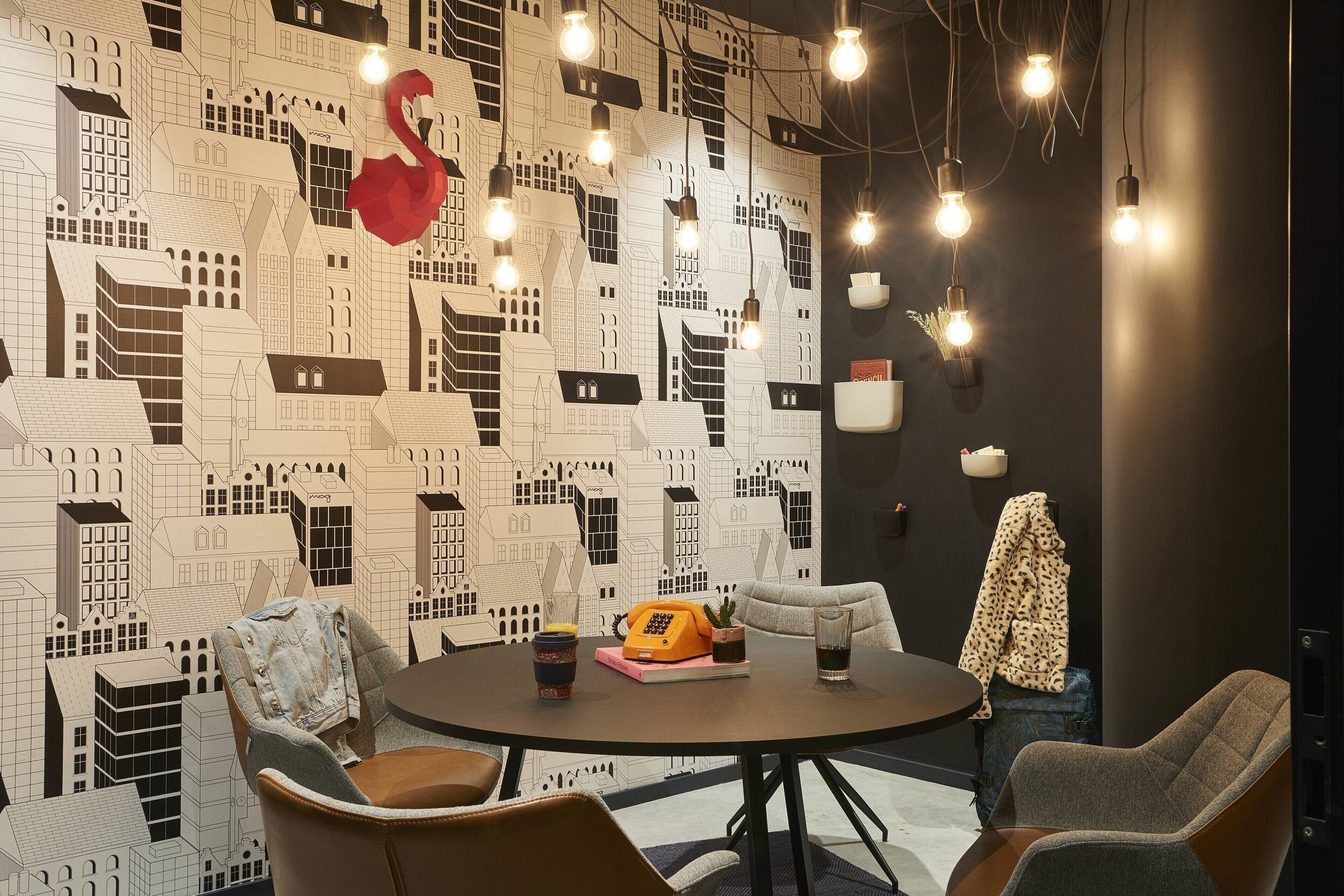 A round table with chairs, a telephone, and a vase of flowers in a modern room with a cityscape wallpaper.