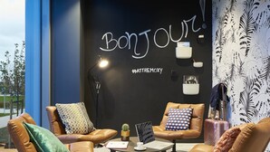 A modern lounge area with leather sofas, a laptop, a small cactus, and a wall with 'BONJOUR' signage and a hashtag.