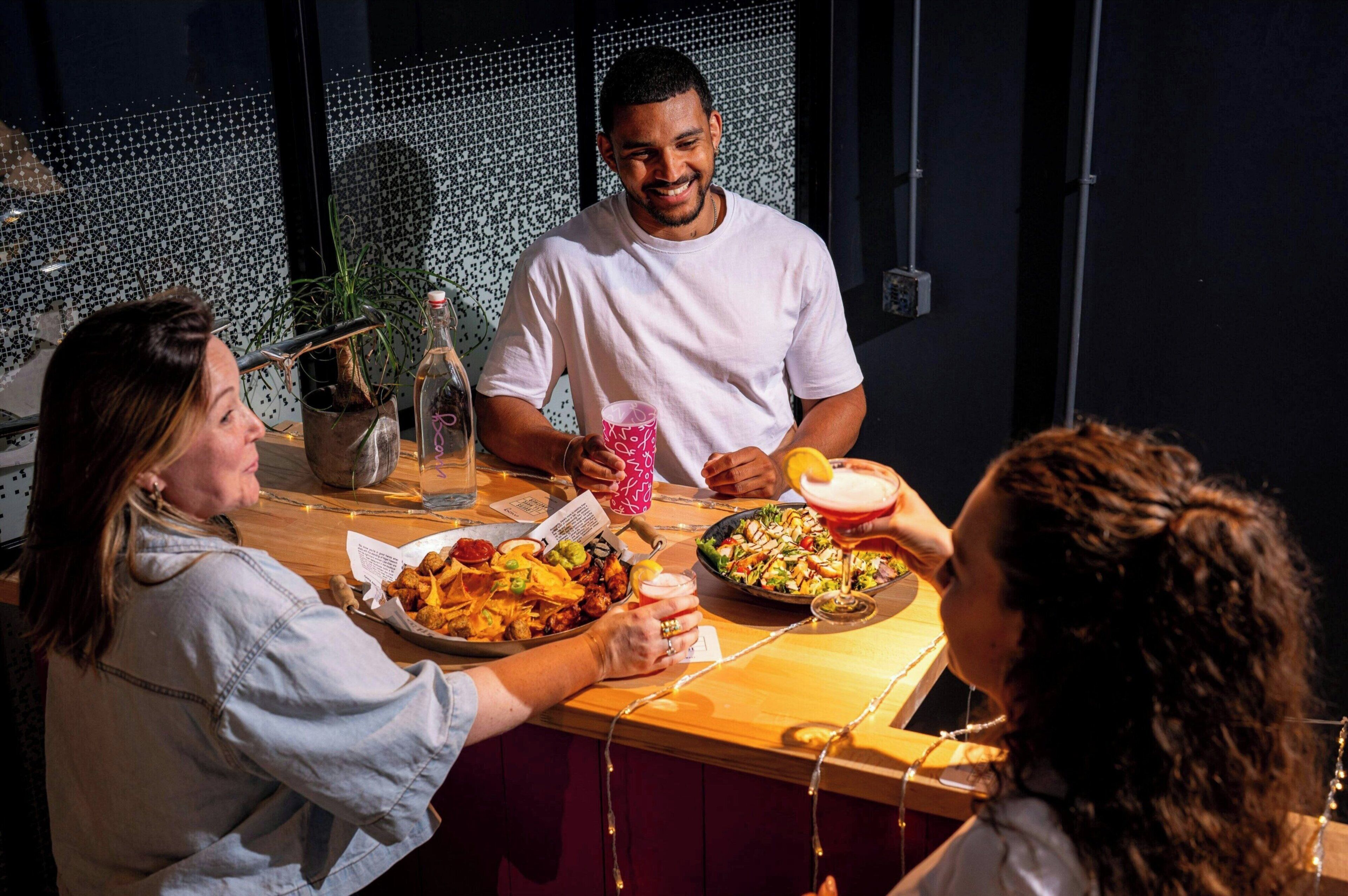 A group of people dining at a restaurant with a tiled wall and string lights in the background.