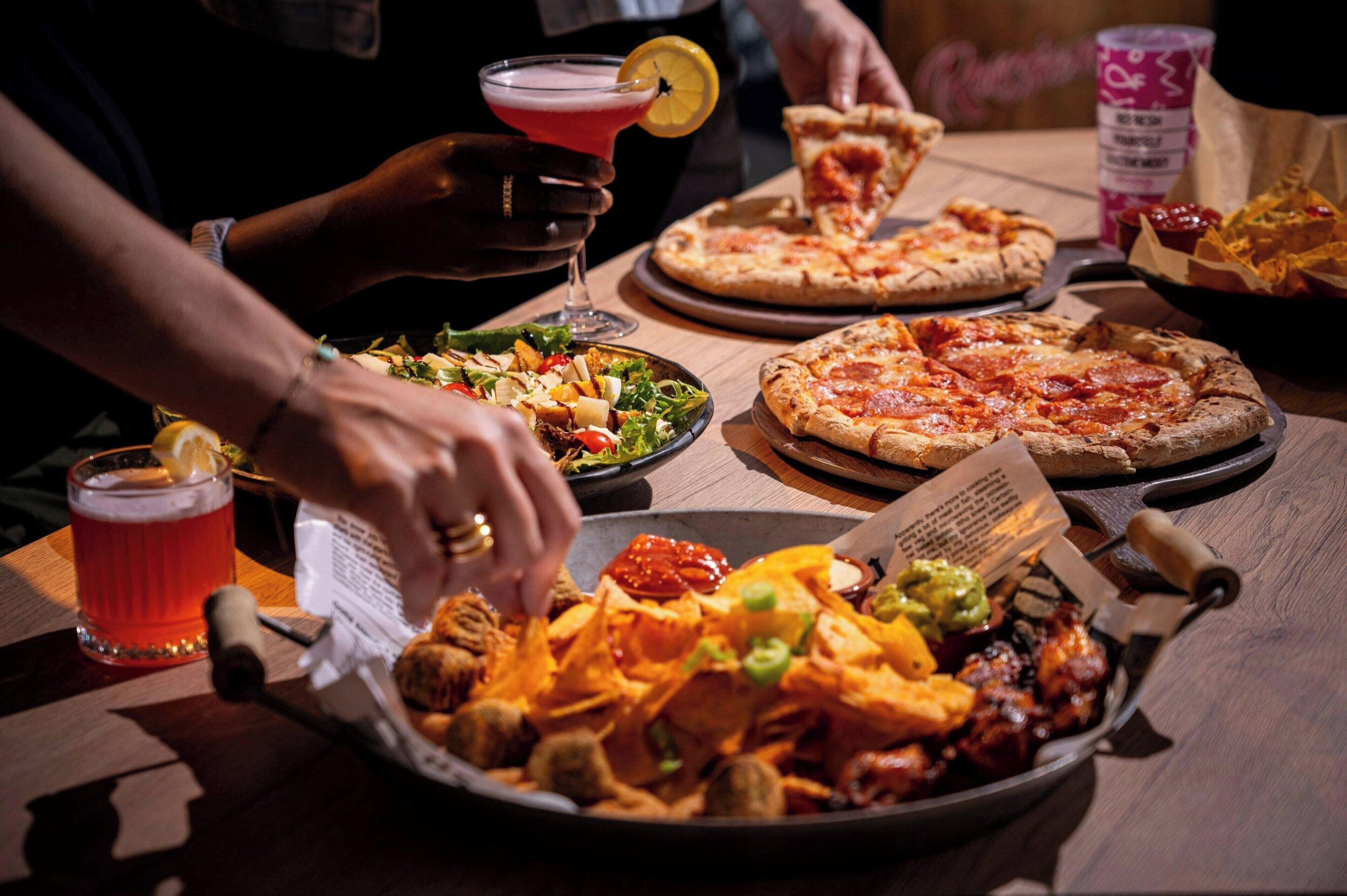 A dining table with a pizza, a salad, nachos, and a drink.