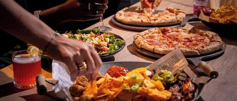 A dining table with a pizza, a salad, nachos, and a drink.