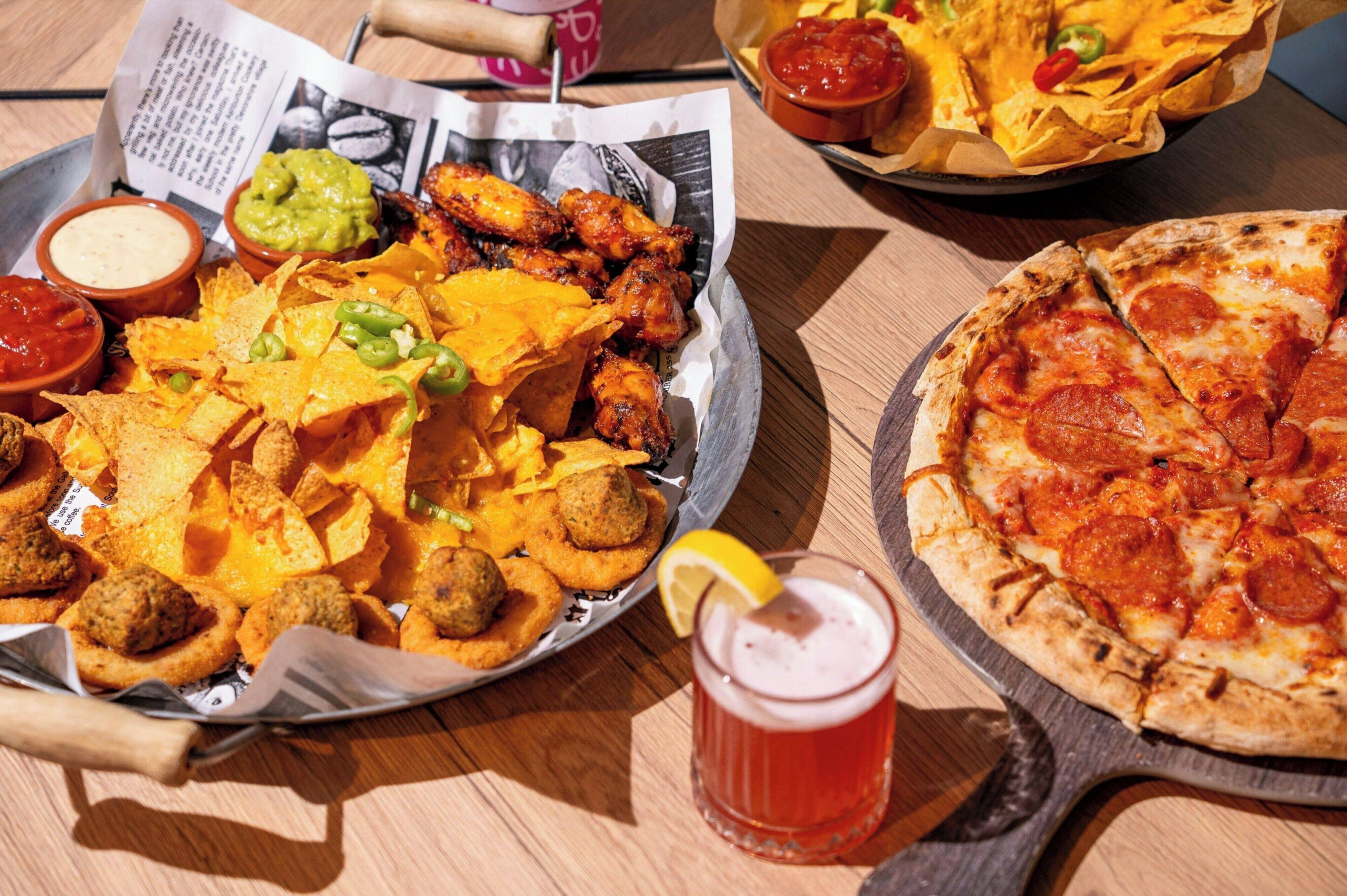 A meal with nachos, meatballs, and a pizza on a wooden table.