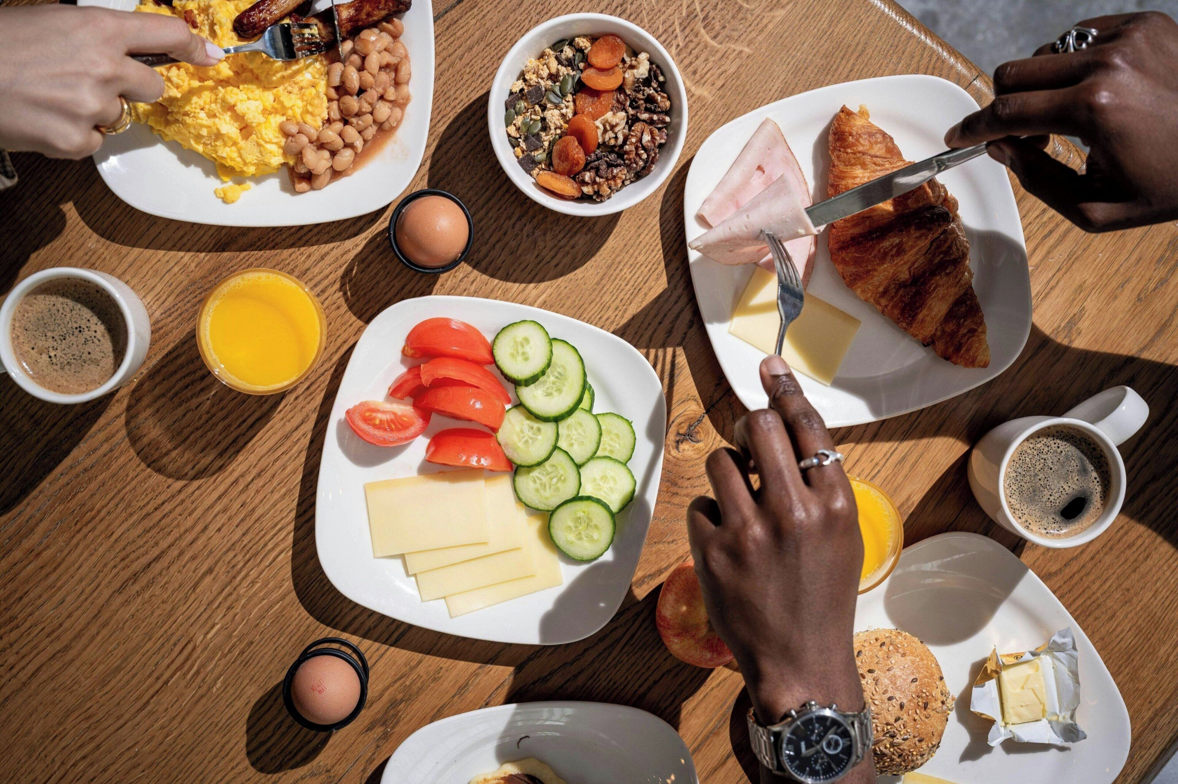 A breakfast setting with plates of food, a coffee cup, and a watch on a wrist.