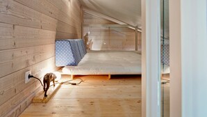 A small, wooden-paneled attic bedroom with a single bed, a power outlet, and a dog standing near the outlet.