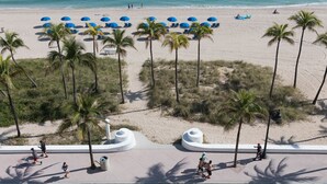 A beach with palm trees, blue umbrellas, and a sandy shore.