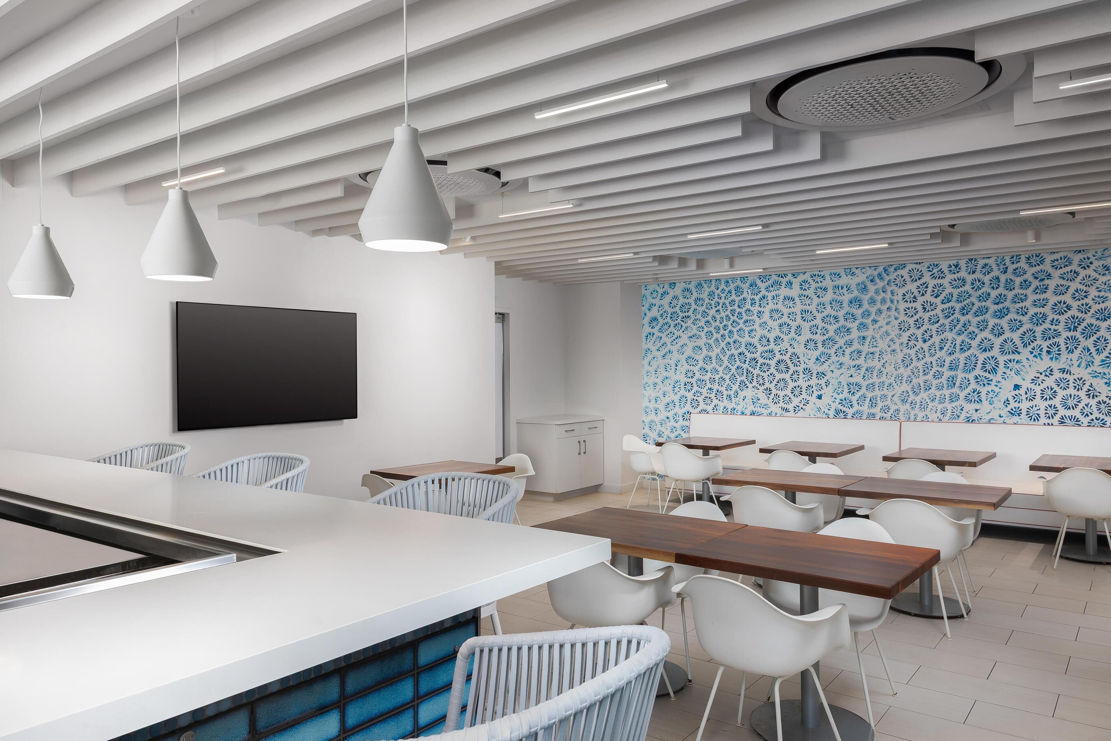 A modern dining area with white chairs, a long wooden table, pendant lights, and a patterned wall.