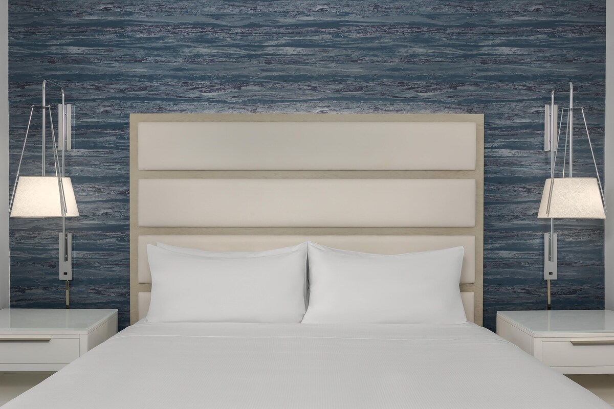 Een bed met witte lakens, een houten hoofdbord en twee nachtkastjes met lampen.