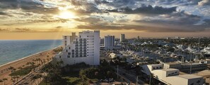 Een kuststadsgezicht met een opvallend hotel in modern design, een jachthaven met veel boten en een strand met palmbomen.