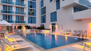 A modern hotel with a swimming pool, sun loungers, and a large building with balconies.