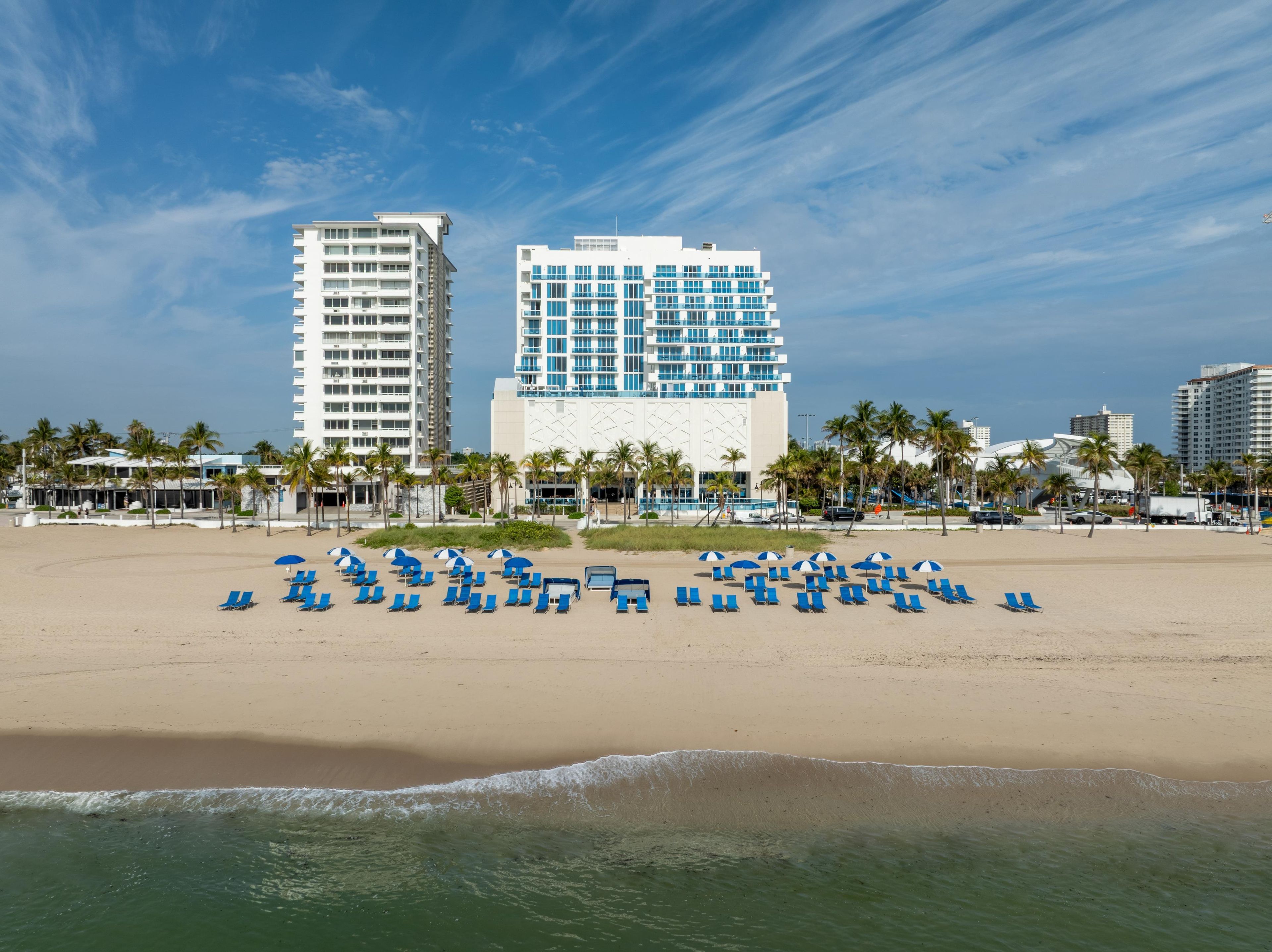 A beachfront hotel with multiple floors, a pool area, and a beach with sun loungers.