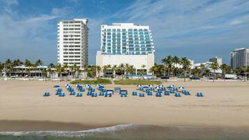 A beachfront hotel with multiple floors, a pool area, and a beach with sun loungers.
