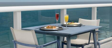 A dining table with two plates of food, two glasses of beverages, and a view of the sea.