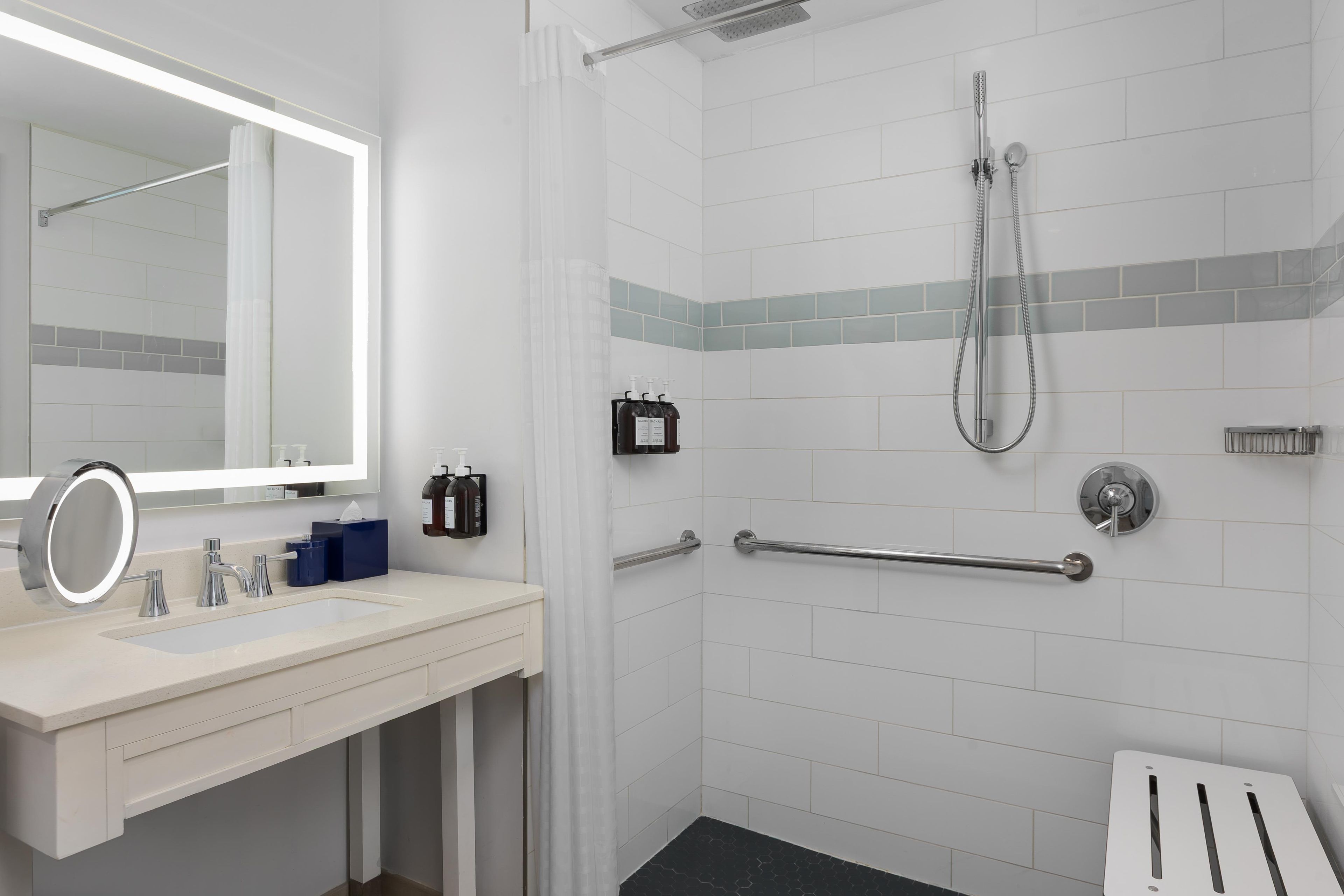 A bathroom with a sink, mirror, shower, and grab bars.