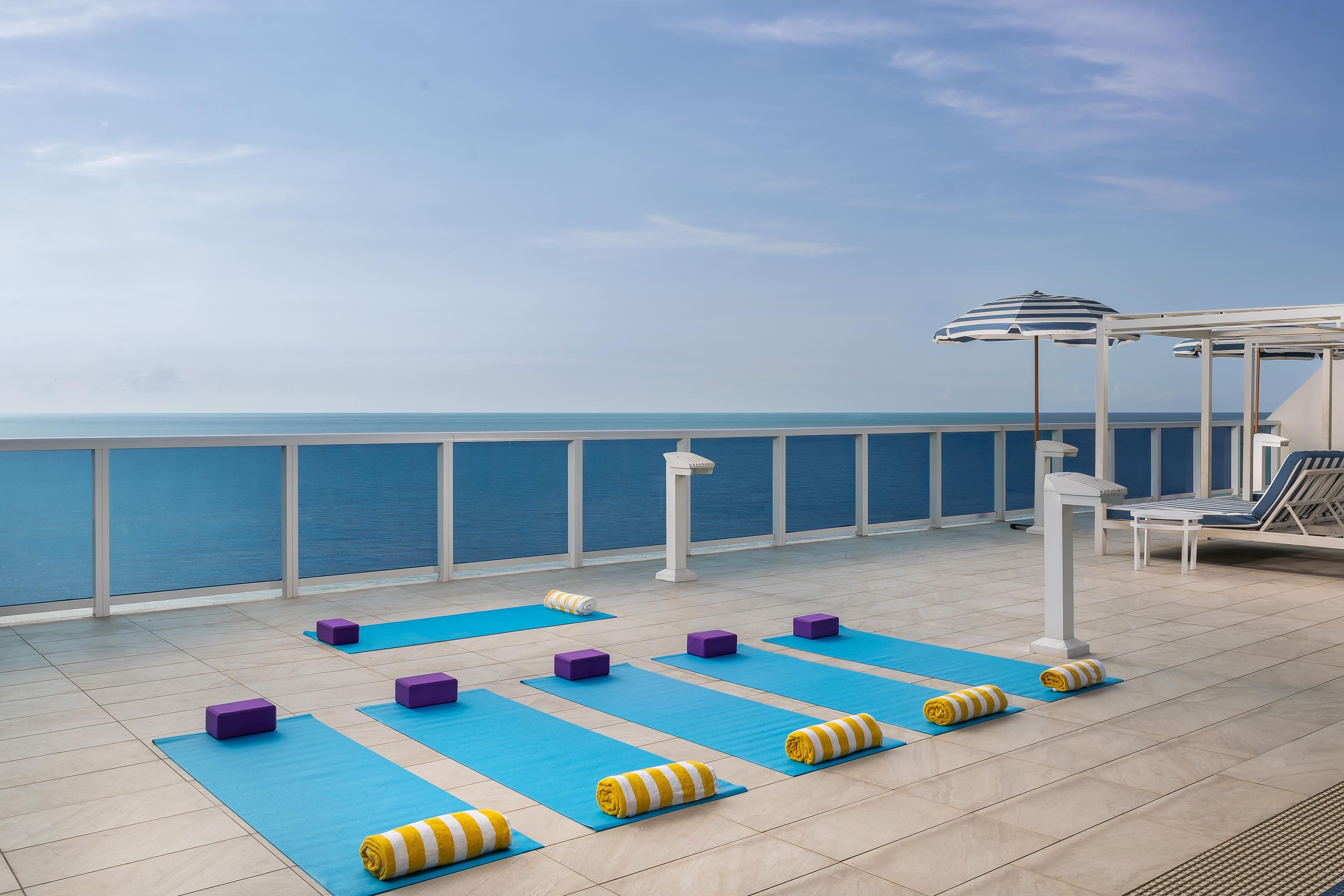 Terraza con colchonetas de ejercicio, bloques de yoga y toallas, con vista a una masa de agua.