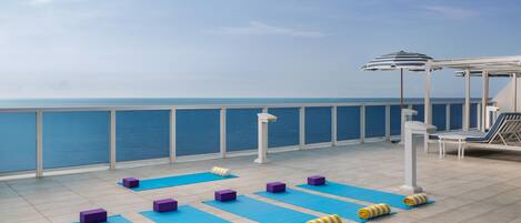 Terraza con colchonetas de ejercicio, bloques de yoga y toallas, con vista a una masa de agua.