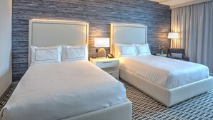 A hotel room with two beds, a nightstand with a lamp, a chair, and a wall with a textured pattern.