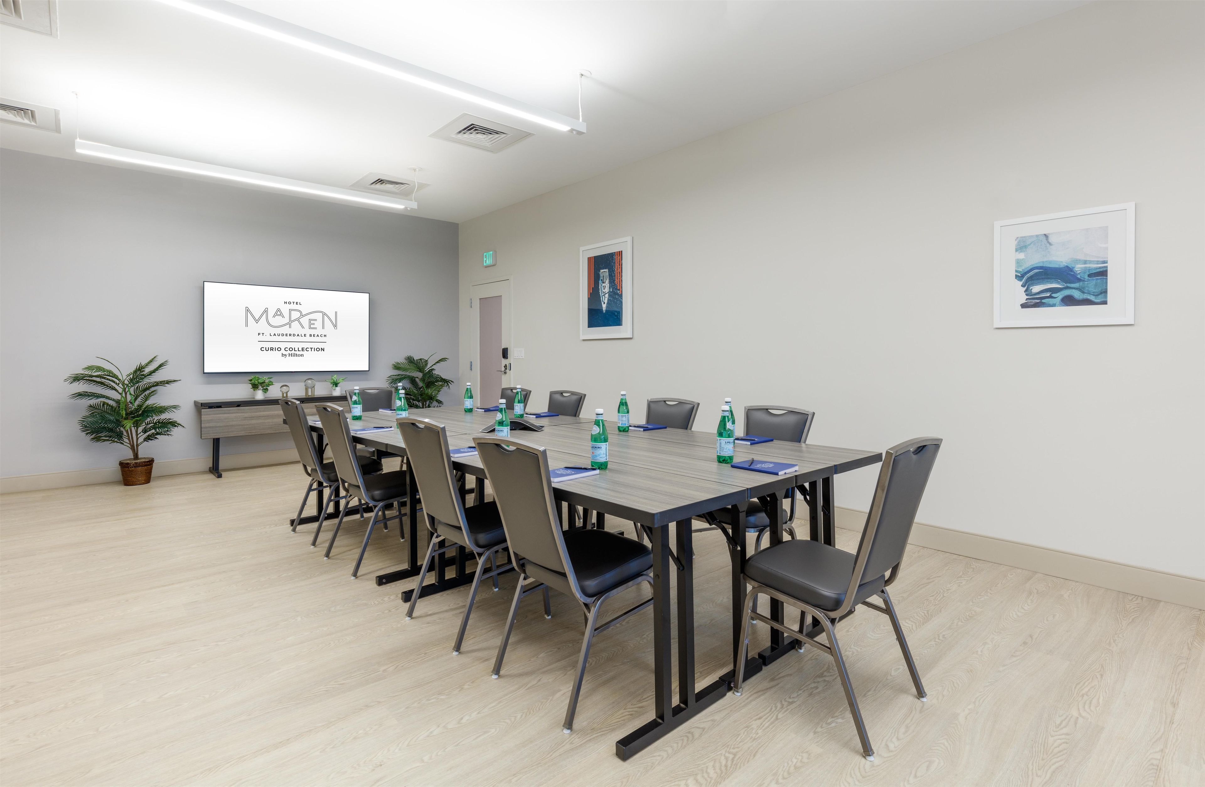 A conference room with a long table, chairs, a projector screen, and a door.