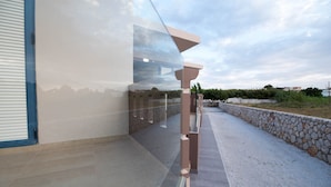 A modern building with a glass facade, a stone wall, and a paved terrace. - Electra Studios (Platanias)