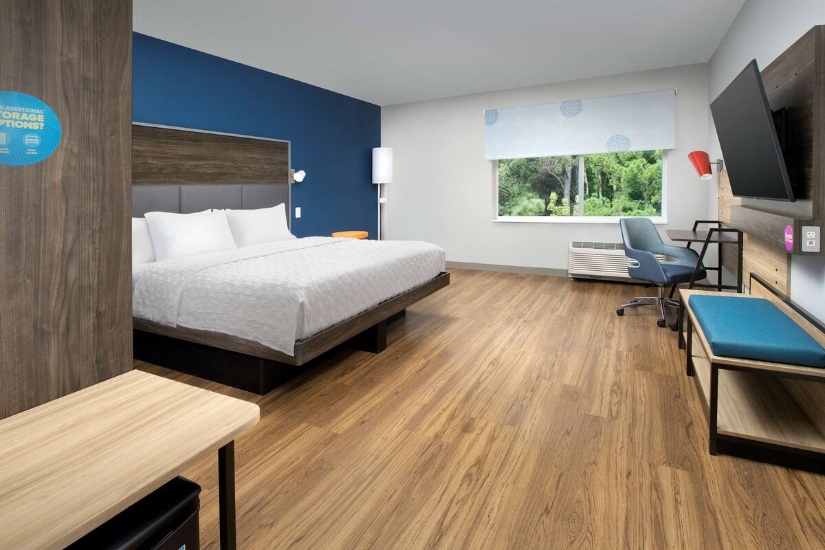 Een moderne hotelkamer met een bed, een bureau, een stoel, een televisie en een raam met uitzicht op groen.