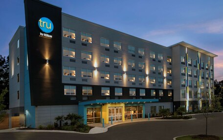 A modern hotel building with a prominent 'tru by Hilton' sign, multiple floors, and a well-lit entrance.