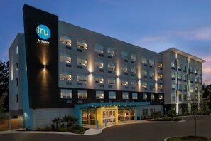 A modern hotel building with a prominent 'tru by Hilton' sign, multiple floors, and a well-lit entrance.