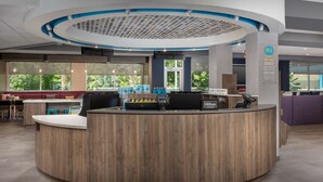 Een moderne hotelontvangst met een houten receptiebalie, een zithoek en grote ramen met uitzicht op de omgeving.