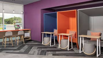 A modern office space with a desk, two chairs, a computer, and a seating area with a couch and ottoman.