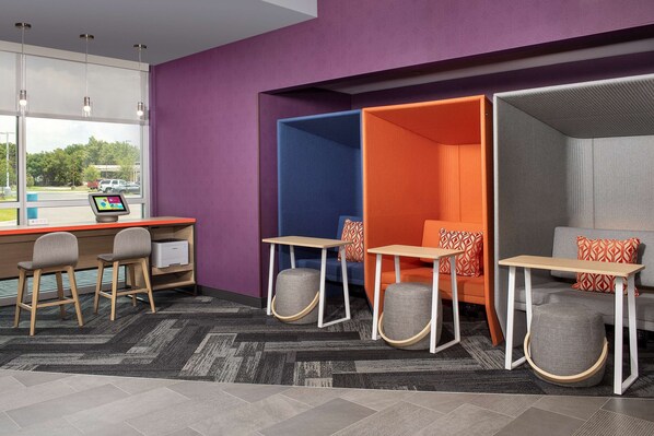 A modern office space with a desk, two chairs, a computer, and a seating area with a couch and ottoman.