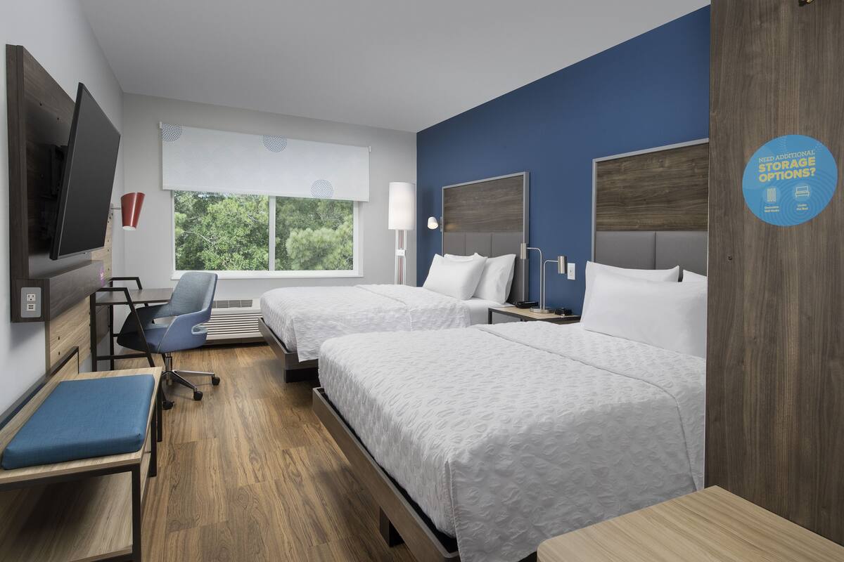 Hotelkamer met twee bedden, een bureau, een stoel, een televisie en een raam met uitzicht op bomen.