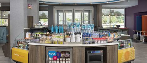 A modern self-service beverage station with a variety of drinks and snacks, a refrigerated section, and a digital payment terminal.