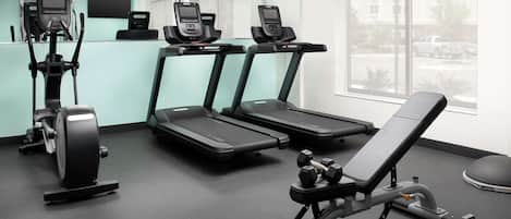Un gimnasio con cintas de correr, elípticas y una prensa de pesas.