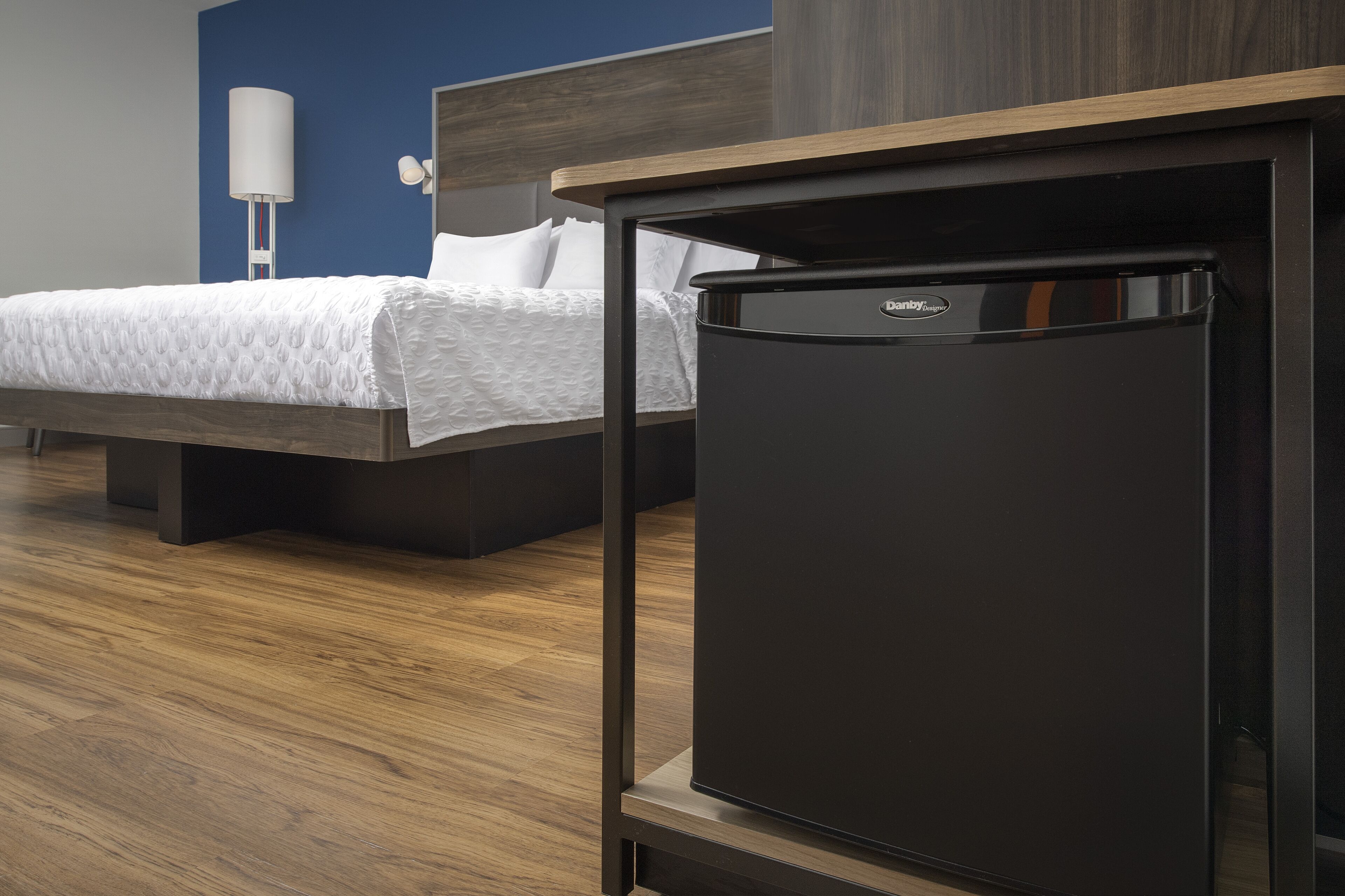 A modern hotel room with a bed, a black minibar, and a wooden floor.