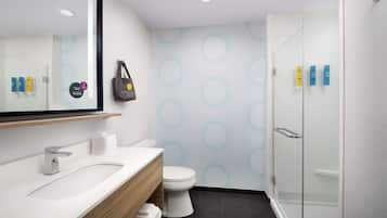 Un baño moderno con un lavamanos blanco, inodoro y cabina de ducha con paredes de vidrio. Hay artículos de aseo en la pared y un bolso colgado.