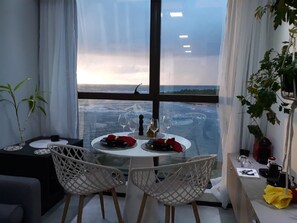Ein Essbereich mit Tisch für zwei Personen, Meerblick und einer Pflanze auf der Fensterbank.