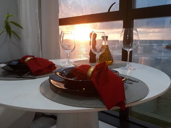 A dining table with a view of the sunset over the water, two wine glasses, and a bottle of wine. - FlatBeachBarra - Love Island - Paiva Beach (Barra de Jangada)