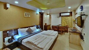 A hotel room with two beds, a desk, a chair, a television, and an air conditioning unit. - Hotel Shree Vatika (Bhopal)