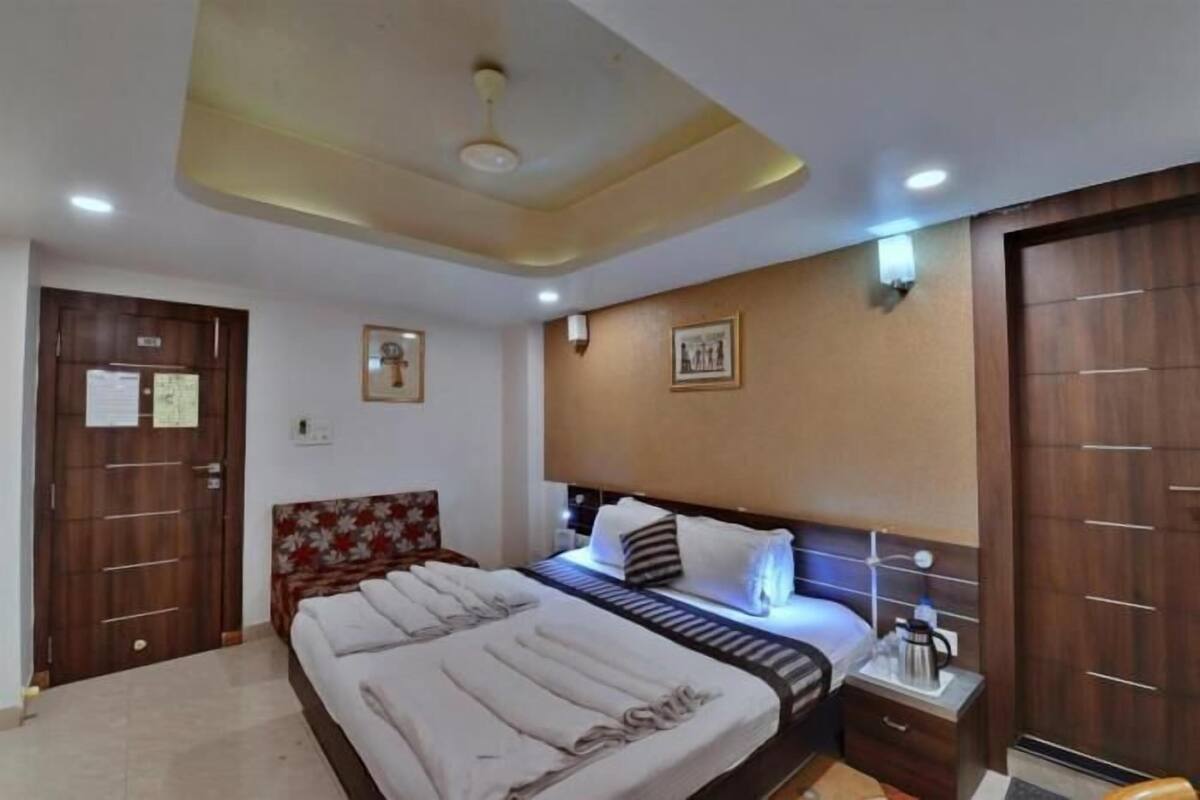 A hotel room with a bed, bedside table, wall-mounted light, and a ceiling fan.